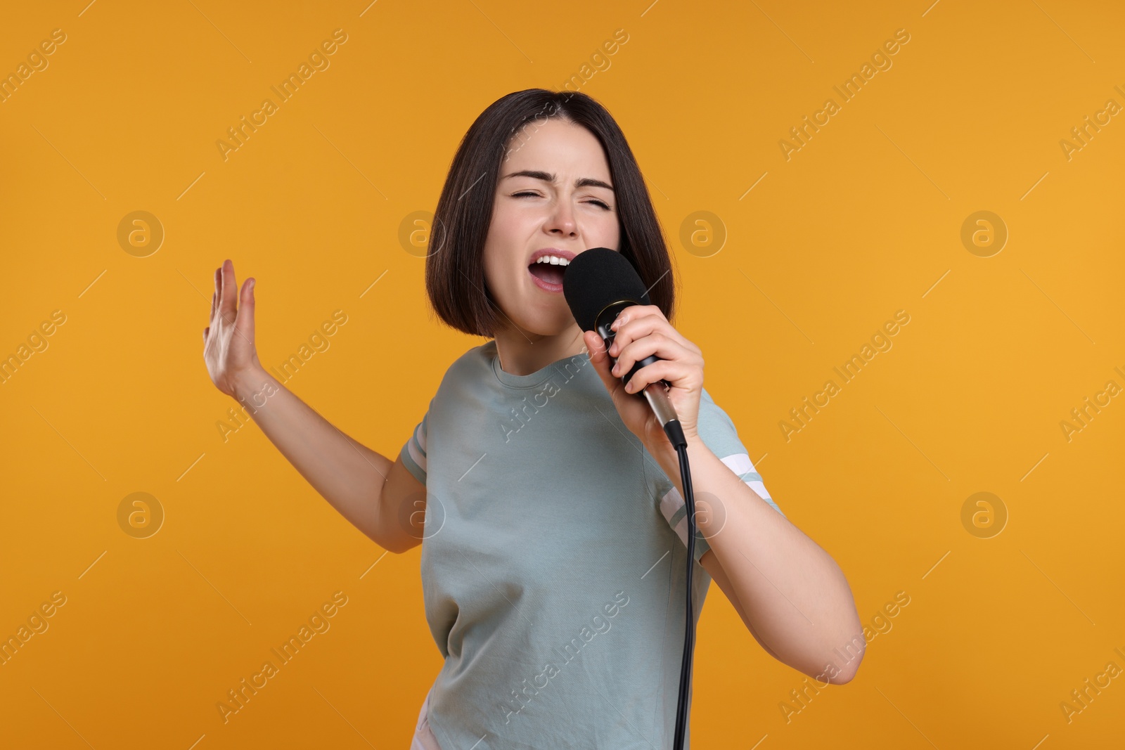 Photo of Beautiful young woman with microphone singing on yellow background