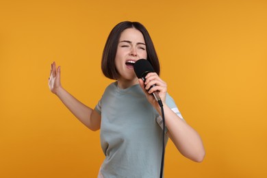 Beautiful young woman with microphone singing on yellow background