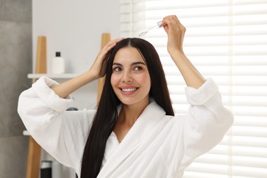 Beautiful woman applying hair serum in bathroom. Cosmetic product