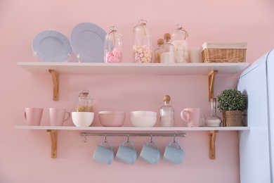 Photo of Shelves with dishware and products on pink wall in kitchen