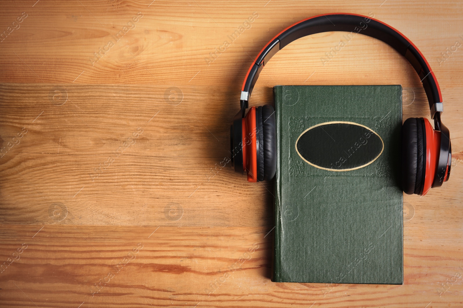 Photo of Book and modern headphones on wooden table, top view. Space for text