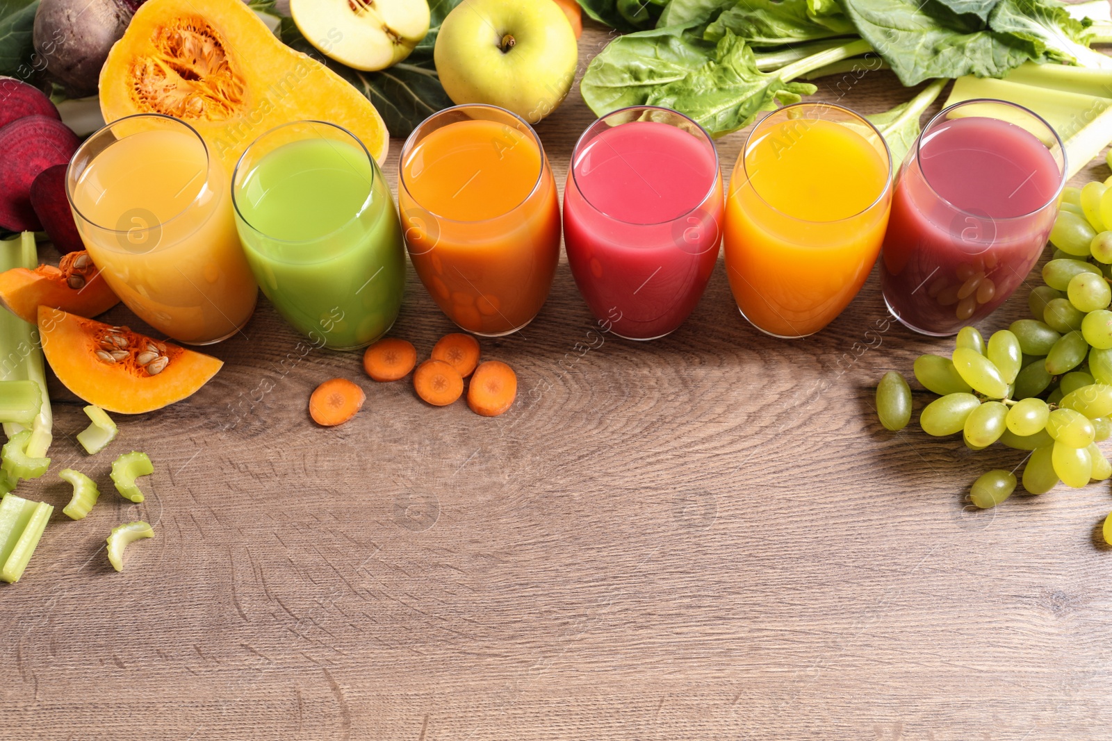 Photo of Glasses with different juices and fresh ingredients on wooden table. Space for text