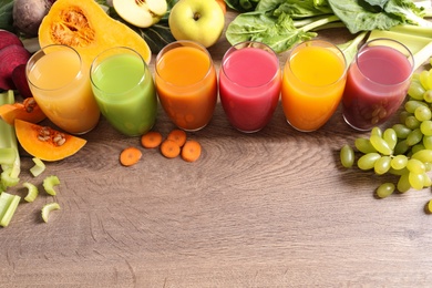 Glasses with different juices and fresh ingredients on wooden table. Space for text