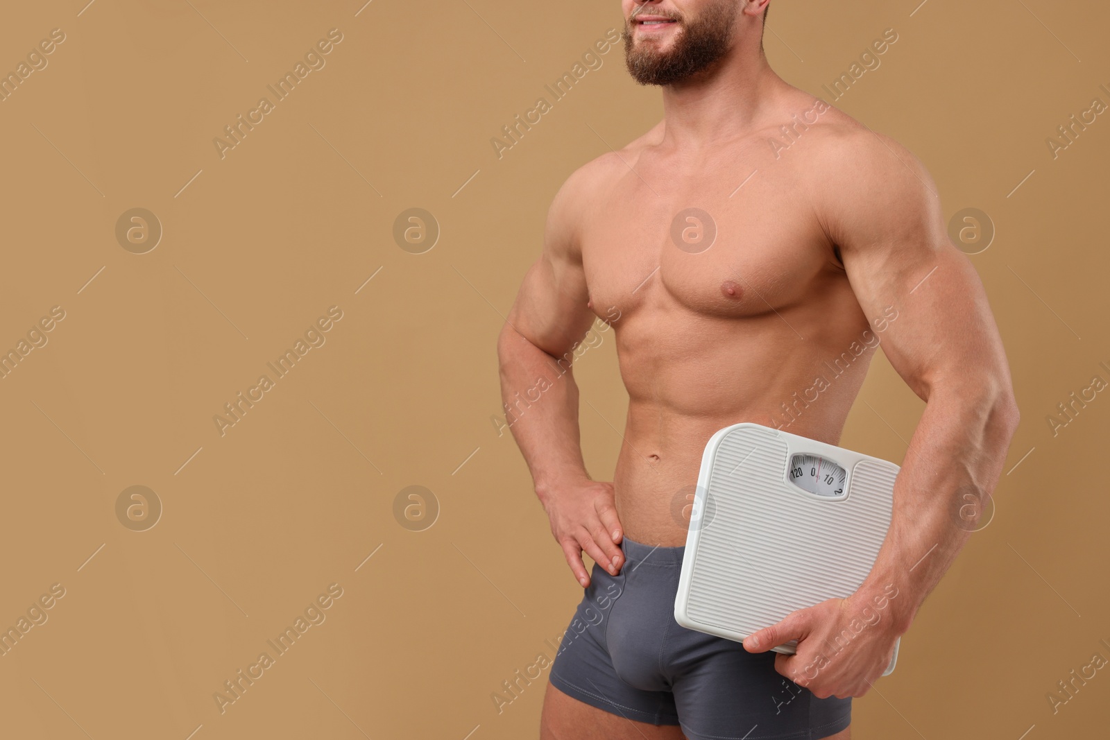 Photo of Athletic man holding scales on brown background, closeup and space for text. Weight loss concept