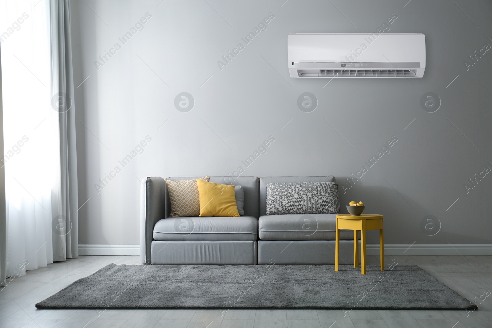 Image of Modern air conditioner on light grey wall in living room with stylish sofa