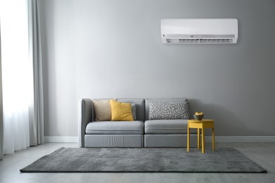 Modern air conditioner on light grey wall in living room with stylish sofa