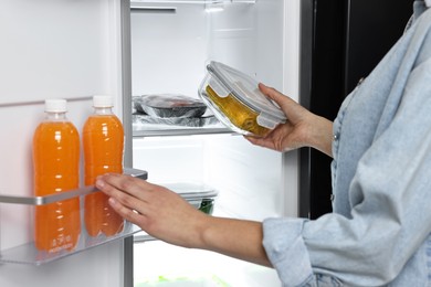 Photo of Young woman taking container with corn out of refrigerator, closeup