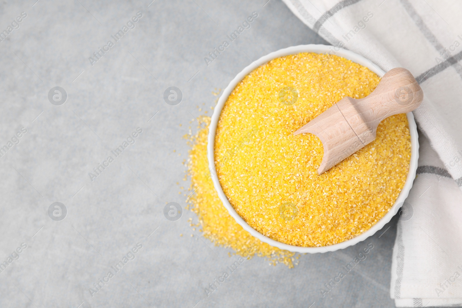 Photo of Raw cornmeal and scoop in bowl on grey table, top view. Space for text