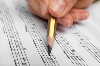 Photo of Woman writing music notes on sheet with pencil, closeup