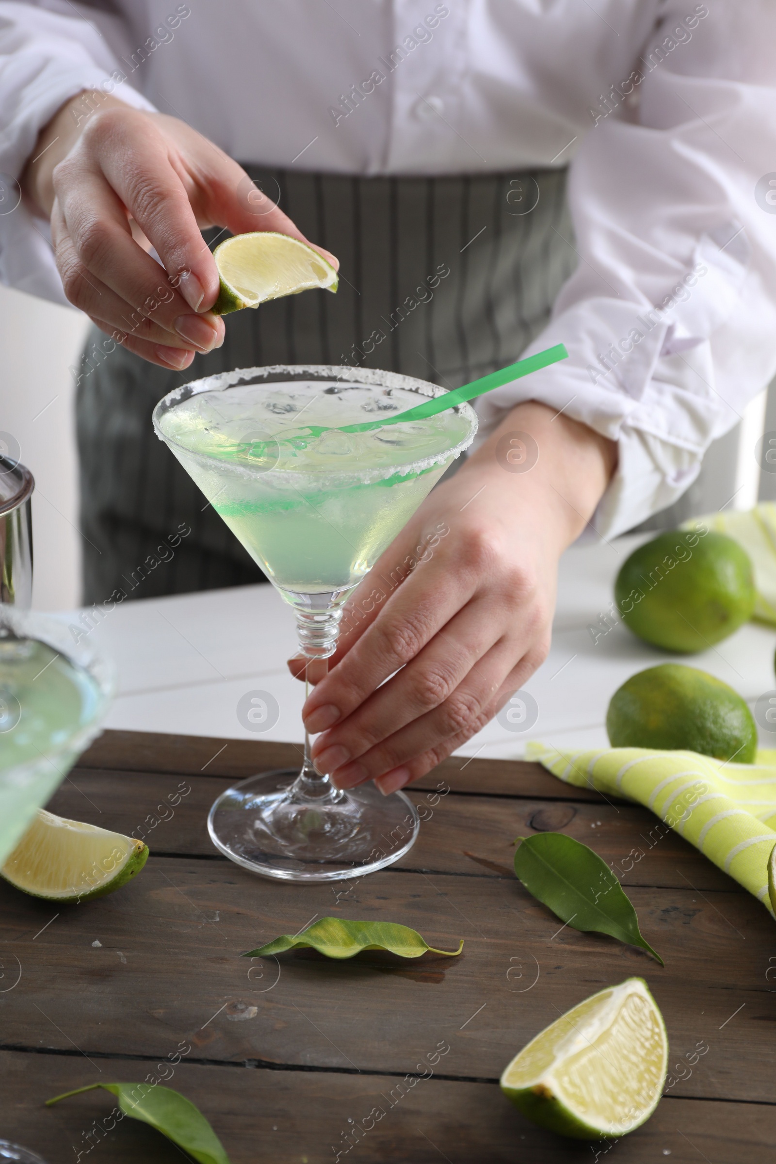 Photo of Bartender squeezing lime juice into glass with delicious Margarita cocktail at wooden table, closeup