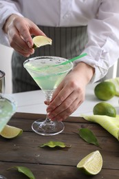 Bartender squeezing lime juice into glass with delicious Margarita cocktail at wooden table, closeup