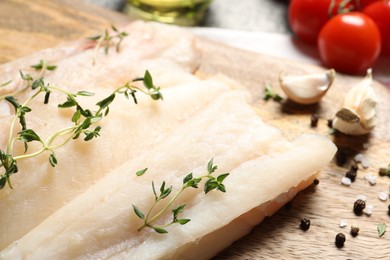 Photo of Board with raw cod fish, microgreens and spices on table, closeup