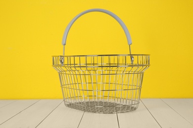 Empty metal shopping basket on white wooden table against yellow background