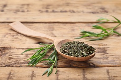 Spoon of dry tarragon and green leaves on wooden table