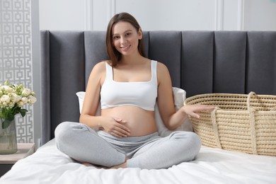 Photo of Beautiful pregnant woman with baby basket on bed indoors