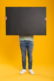 Man holding black blank poster on yellow background. Mockup for design