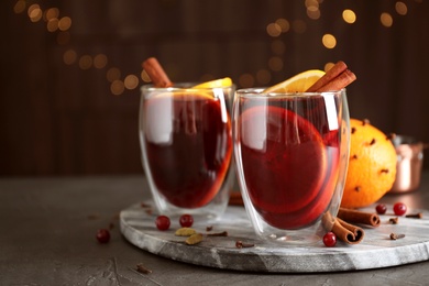 Photo of Glasses of tasty mulled wine on grey table against festive lights