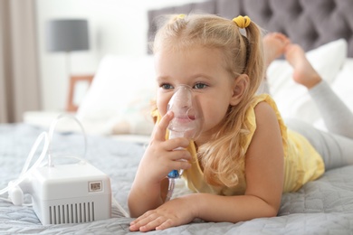 Photo of Little girl using asthma machine in bedroom. Space for text