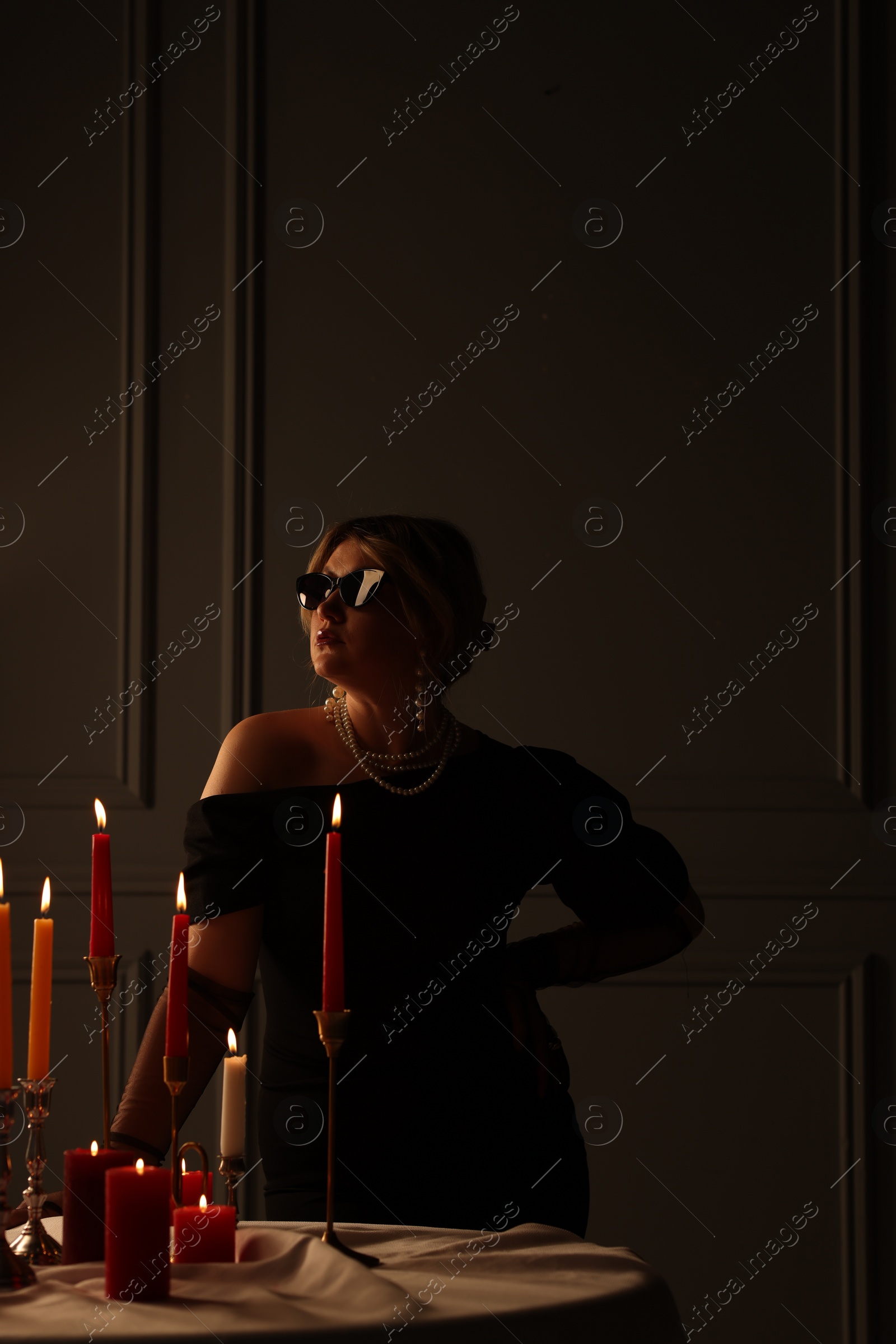 Photo of Beautiful young woman in sunglasses near table with burning candles at night