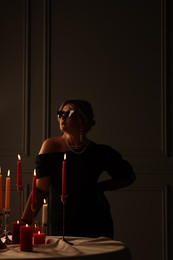 Beautiful young woman in sunglasses near table with burning candles at night