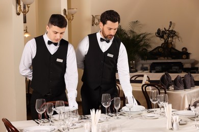 Men setting table in restaurant. Professional butler courses