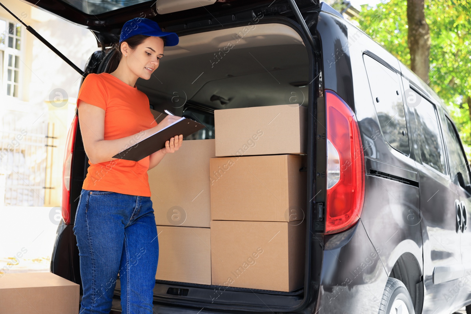 Photo of Courier writing near packages and delivery truck outdoors