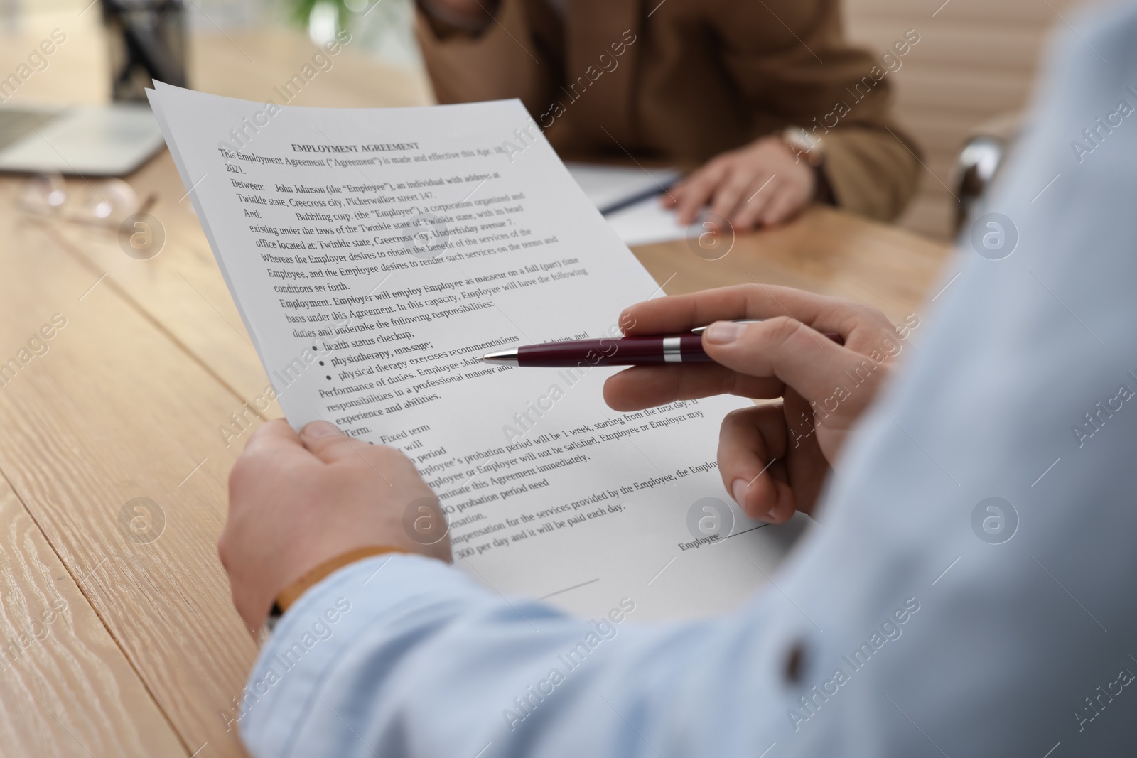 Photo of Man reading employment agreement at table in office, closeup. Signing contract