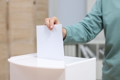 Photo of Woman putting her vote into ballot box on blurred background, closeup