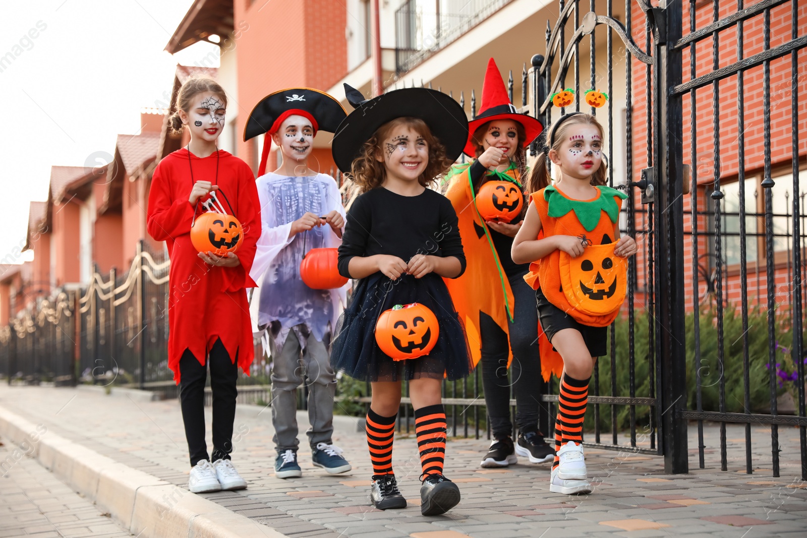 Photo of Cute little kids wearing Halloween costumes going trick-or-treating outdoors