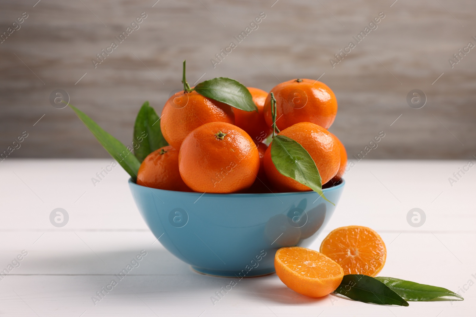 Photo of Bowl with fresh ripe juicy tangerines and green leaves on white wooden table, closeup