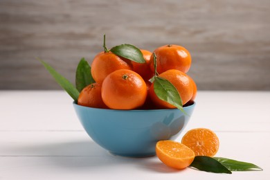 Photo of Bowl with fresh ripe juicy tangerines and green leaves on white wooden table, closeup