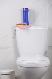 Photo of Bottle, sponge and cleaning rag on toilet bowl in bathroom