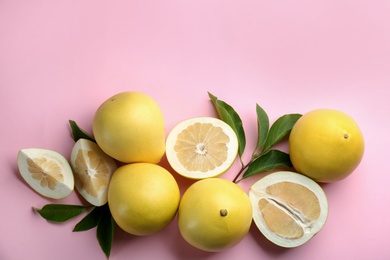 Photo of Fresh cut and whole pomelo fruits with leaves on pink background, flat lay. Space for text