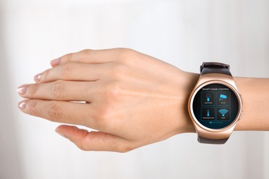 Image of Woman wearing smartwatch with icons of smart home control app on display against light background, closeup