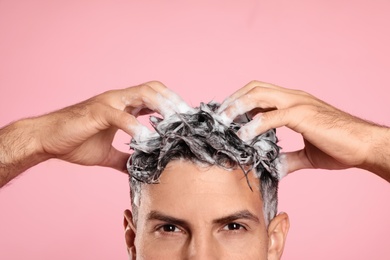 Photo of Handsome man washing hair on pink background, closeup