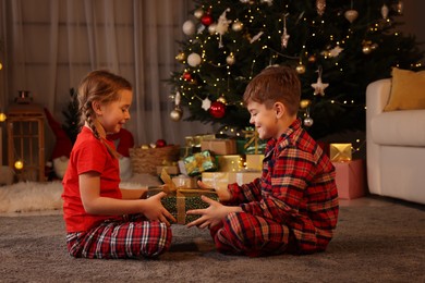 Cute little children with gift box near Christmas tree at home