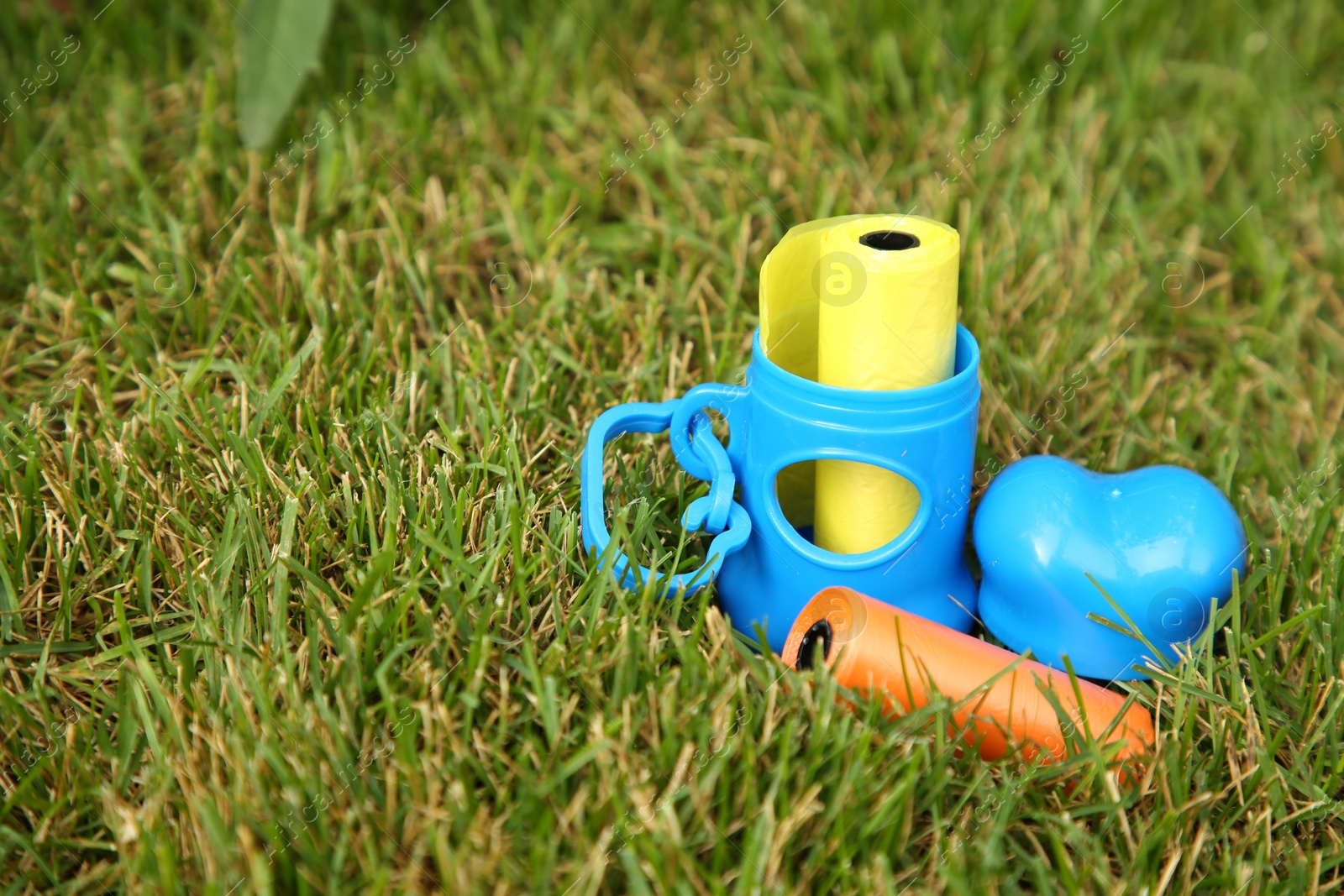 Photo of Rolls of colorful dog waste bags on green grass outdoors, space for text