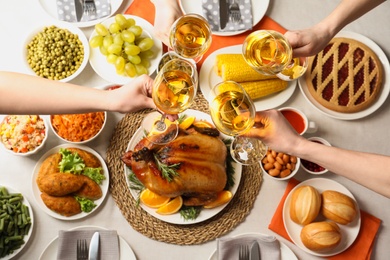 Photo of People holding glasses of wine over table with festive dinner and roasted turkey, top view