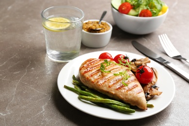 Photo of Tasty grilled chicken fillet with green beans and tomatoes on brown marble table