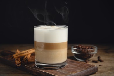 Delicious latte macchiato, cinnamon sticks and coffee beans on wooden table