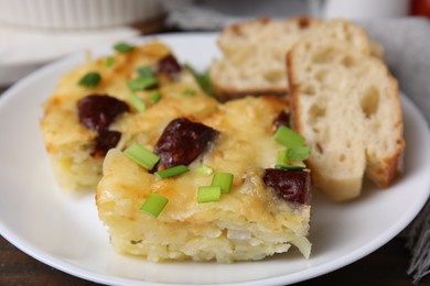 Photo of Tasty sausage casserole with green onion and bread on table, closeup