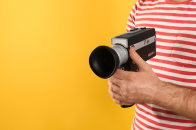 Man with vintage video camera on yellow background, closeup. Space for text