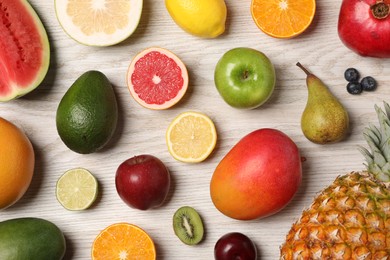 Different ripe fruits and berries on light wooden table, flat lay