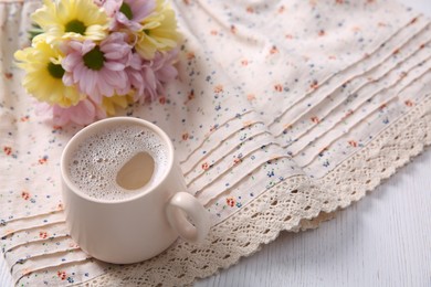 Photo of Cup of fresh coffee and beautiful bouquet on light beige printed cloth, space for text. Good morning