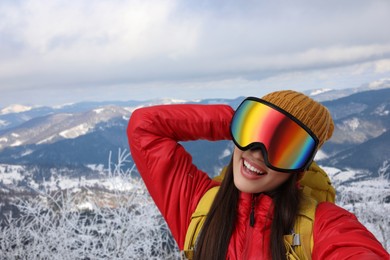 Smiling woman in ski goggles taking selfie in snowy mountains