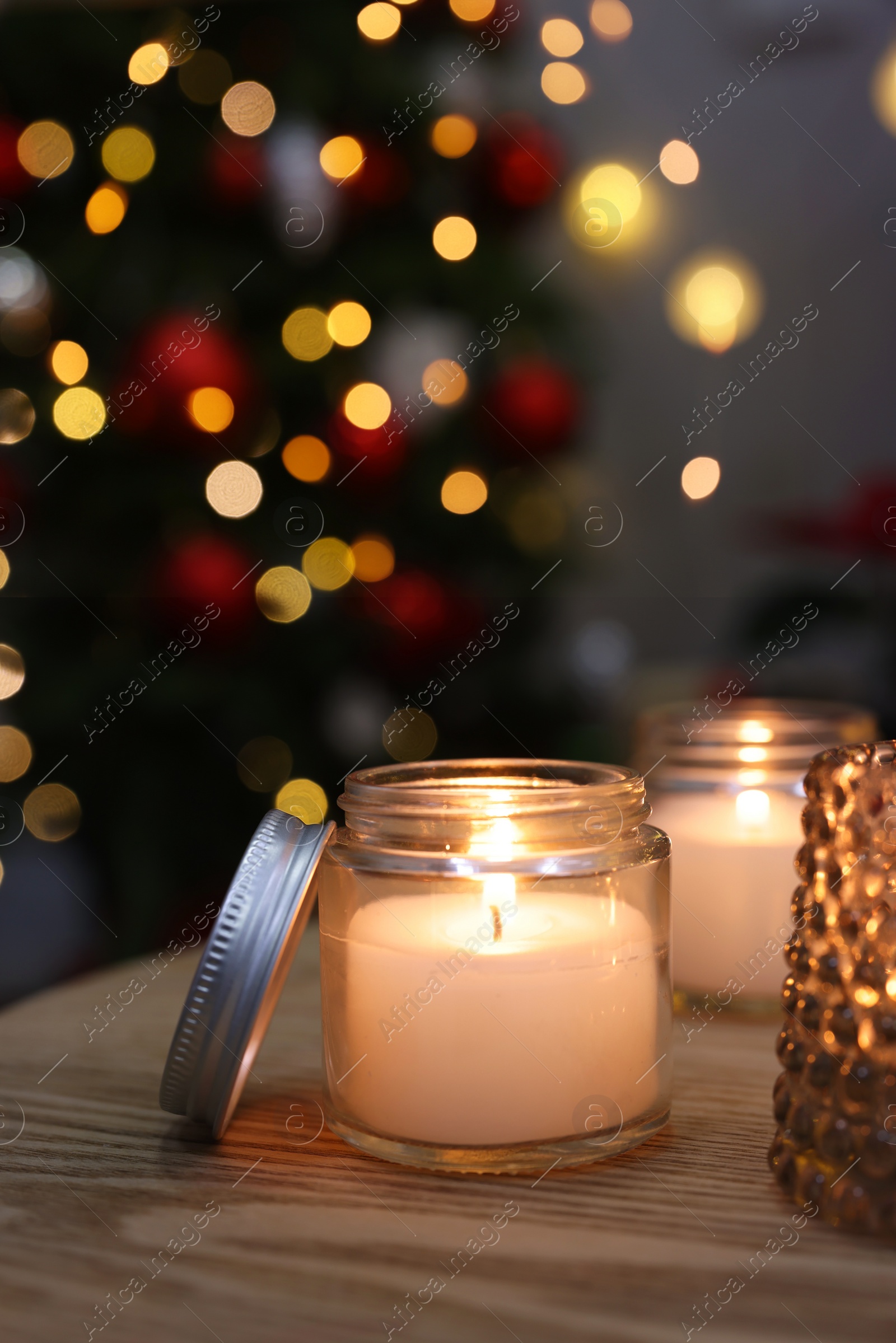 Photo of Burning candles on wooden table in room decorated for Christmas