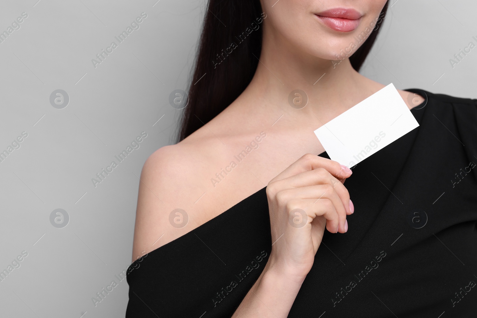 Photo of Woman holding blank business card on light grey background, closeup. Space for text