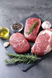 Photo of Raw beef steaks, oil and spices on grey background