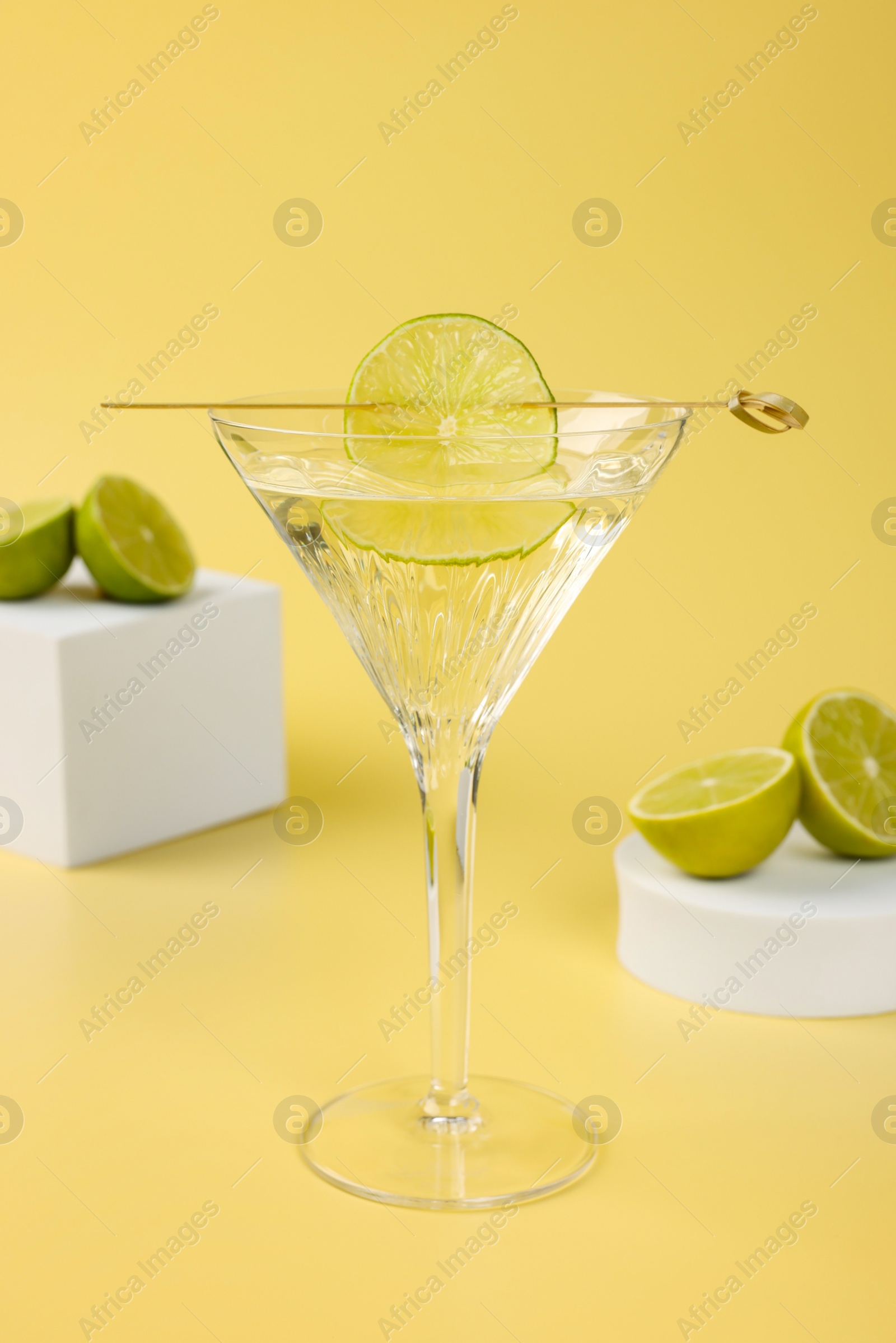 Photo of Martini cocktail with lime slice and fresh fruits on yellow background