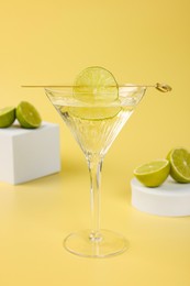 Martini cocktail with lime slice and fresh fruits on yellow background